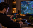 Мужчина делает ставку на киберспорт со смартфона, наблюдая матч по Dota 2 на телевизоре